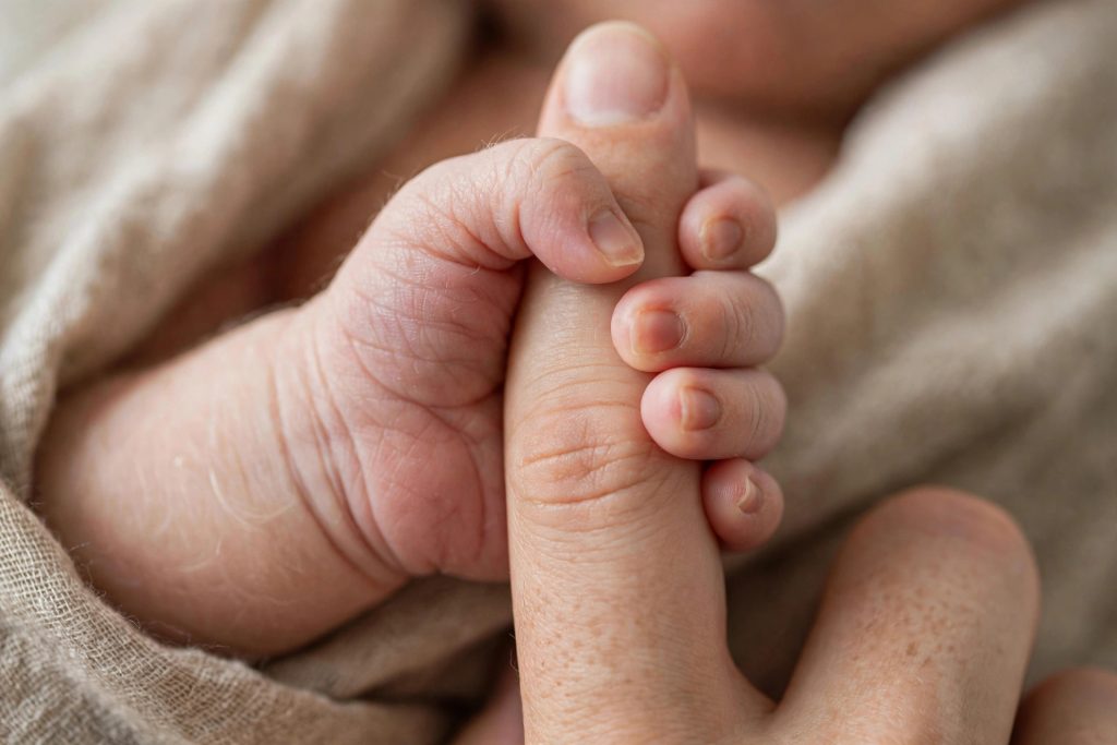 Newborn's hand grasping a parent's finger — palmar grasp reflex